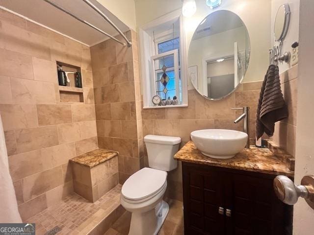 bathroom with decorative backsplash, a tile shower, vanity, tile walls, and toilet