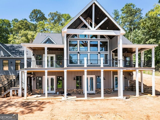 rear view of property with a balcony, french doors, stone siding, a patio area, and board and batten siding