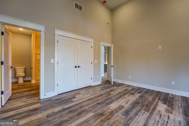 unfurnished bedroom with a high ceiling, dark hardwood / wood-style flooring, and ensuite bathroom