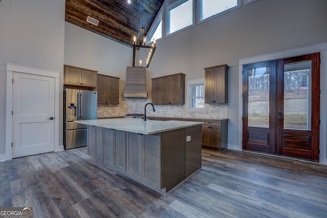 kitchen with visible vents, premium range hood, an island with sink, dark wood-type flooring, and stainless steel fridge