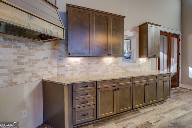 kitchen featuring light wood-type flooring, light stone counters, dark brown cabinetry, and backsplash