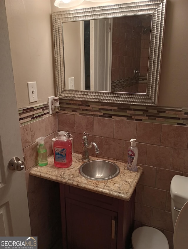 bathroom with toilet, decorative backsplash, vanity, and tile walls