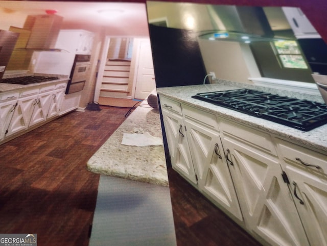 kitchen featuring wall chimney range hood, dark wood-type flooring, light stone countertops, and black gas stovetop