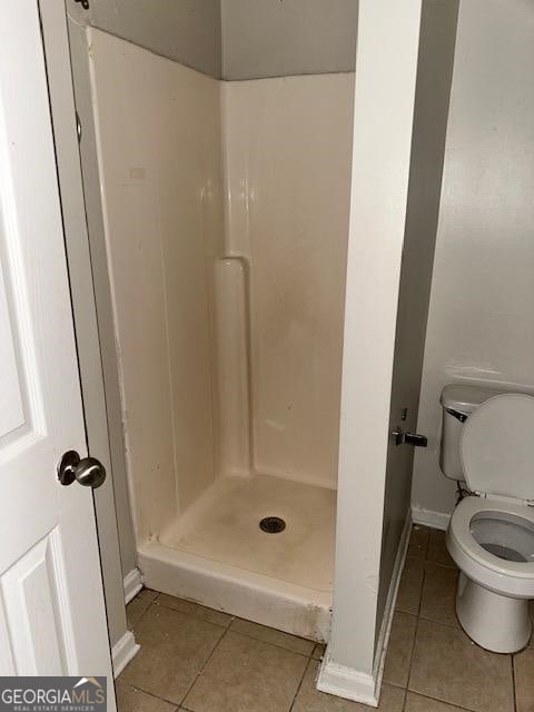 bathroom with a shower, toilet, and tile patterned floors