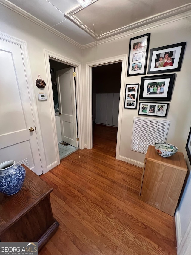 corridor featuring attic access, baseboards, visible vents, ornamental molding, and wood finished floors