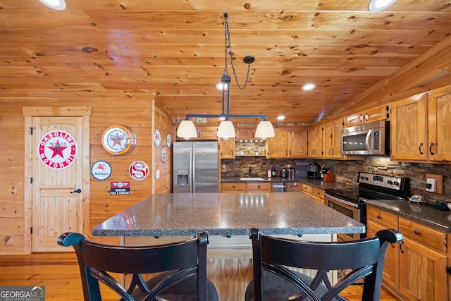 kitchen with decorative light fixtures, appliances with stainless steel finishes, a kitchen island, light wood-type flooring, and wooden walls