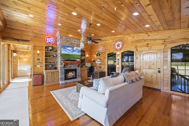 living room featuring wood walls, light hardwood / wood-style floors, ceiling fan, and a fireplace