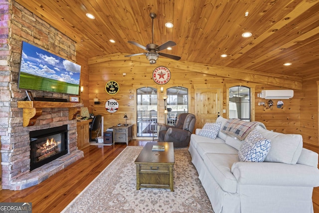 living room with wood walls, hardwood / wood-style flooring, vaulted ceiling, ceiling fan, and a stone fireplace