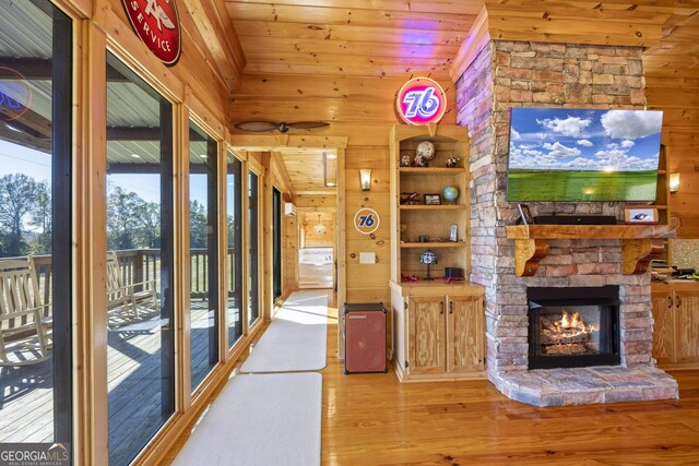 unfurnished living room with light hardwood / wood-style flooring, wood ceiling, wooden walls, and a stone fireplace