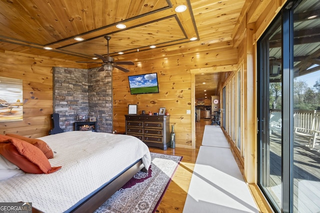 bedroom featuring light hardwood / wood-style flooring, access to outside, a stone fireplace, and wooden ceiling