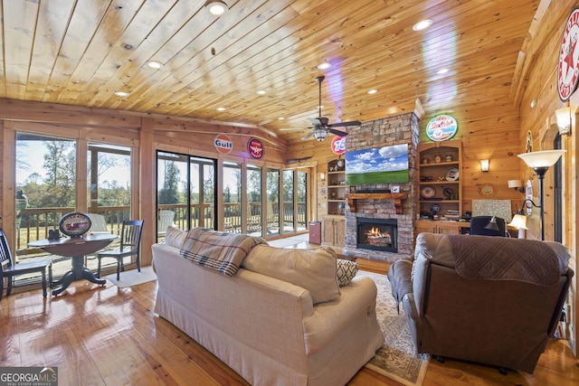 living room with wooden walls, a stone fireplace, and light hardwood / wood-style flooring