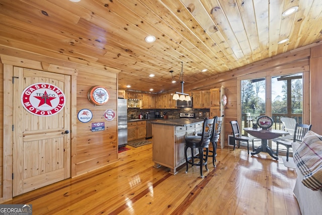 kitchen with decorative light fixtures, appliances with stainless steel finishes, wooden walls, and light hardwood / wood-style floors