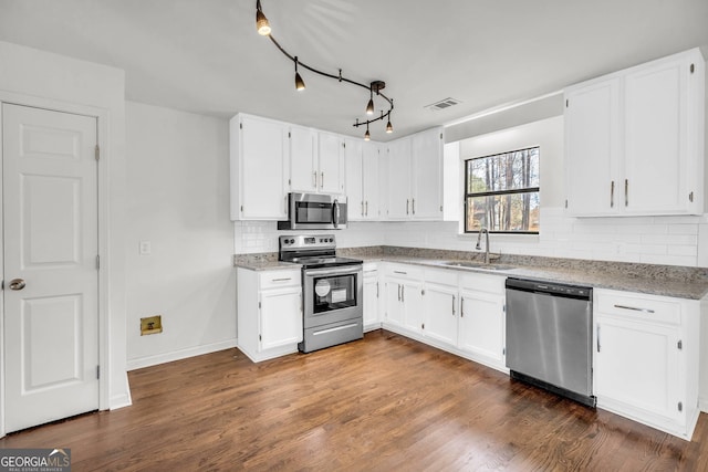 kitchen with appliances with stainless steel finishes, track lighting, light stone countertops, dark hardwood / wood-style floors, and white cabinets