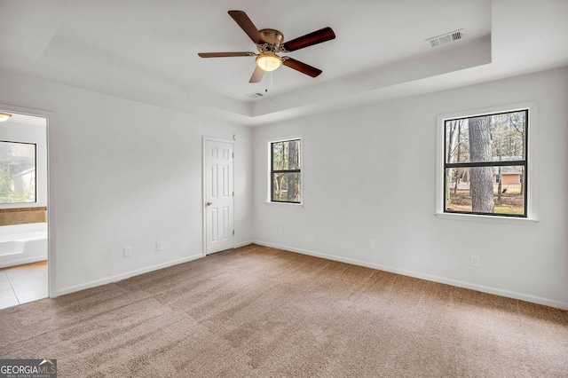 spare room with ceiling fan, light colored carpet, and a tray ceiling