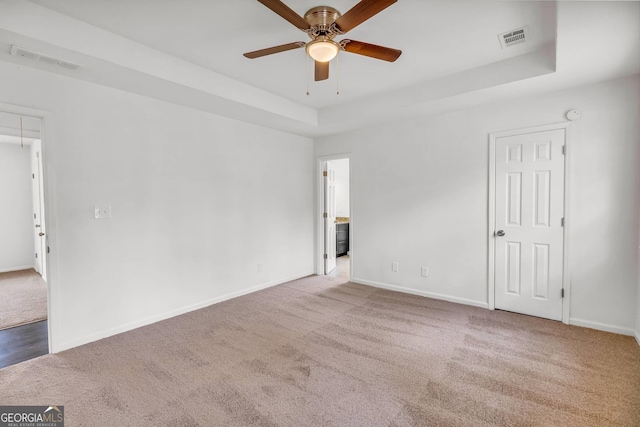 spare room with a tray ceiling, ceiling fan, and light colored carpet