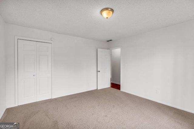 unfurnished bedroom featuring a textured ceiling, dark colored carpet, and a closet