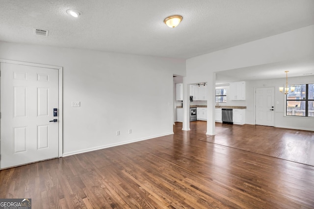 unfurnished living room featuring dark hardwood / wood-style flooring, a notable chandelier, plenty of natural light, and a textured ceiling