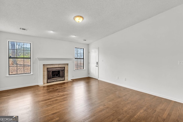 unfurnished living room featuring a tile fireplace, dark hardwood / wood-style floors, and a textured ceiling