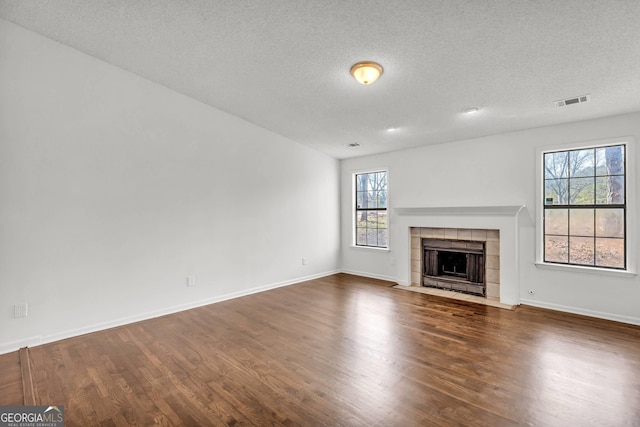 unfurnished living room featuring a tiled fireplace, a textured ceiling, and dark wood-type flooring