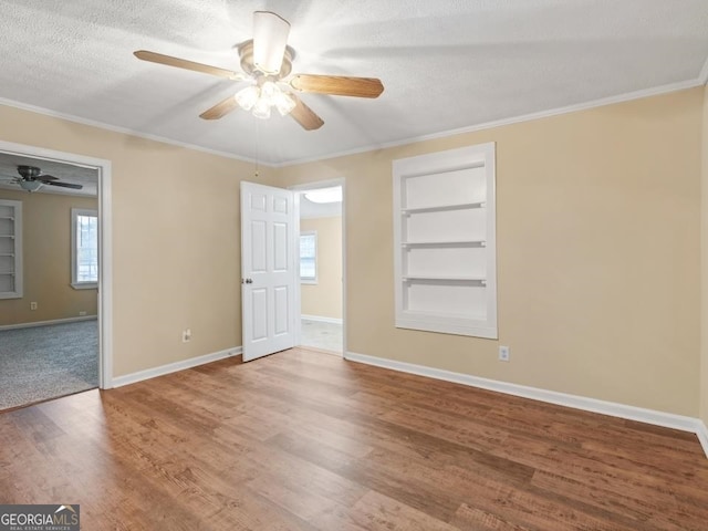 empty room with built in features, ceiling fan, and wood-type flooring