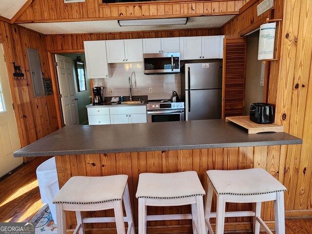 kitchen featuring stainless steel appliances, a breakfast bar, hardwood / wood-style floors, and white cabinetry