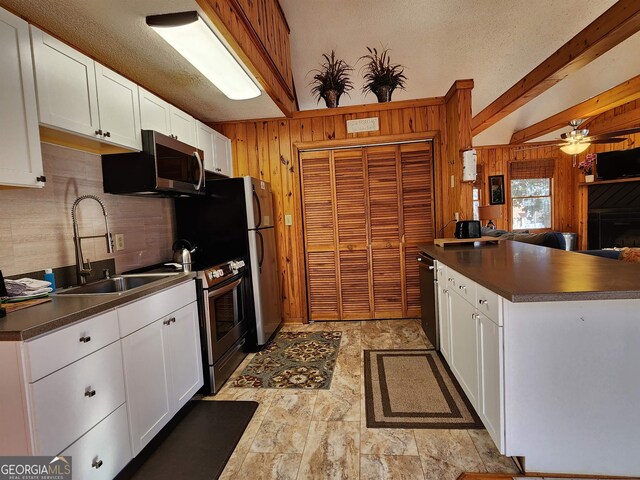 kitchen featuring beam ceiling, sink, wooden walls, white cabinetry, and appliances with stainless steel finishes