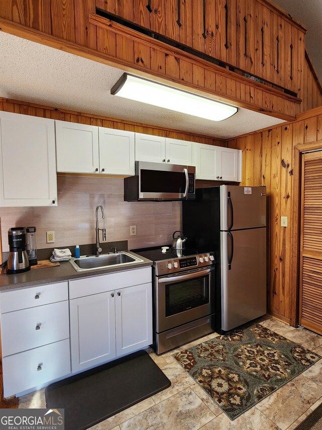 kitchen featuring appliances with stainless steel finishes, wooden walls, sink, and white cabinets