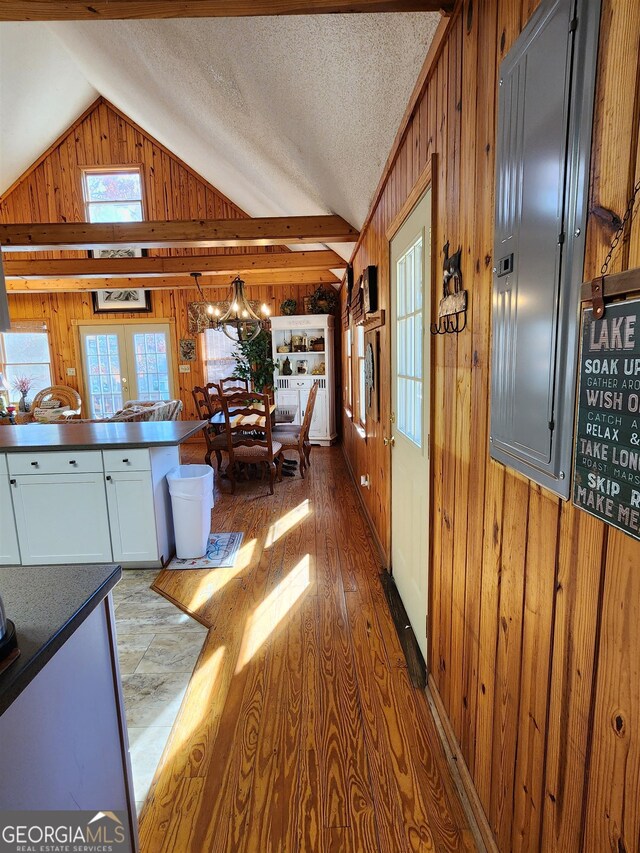 interior space featuring white cabinets, a textured ceiling, lofted ceiling, hardwood / wood-style flooring, and wooden walls