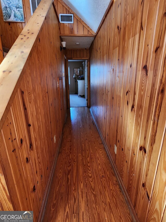 hall featuring wooden walls, vaulted ceiling, and wood-type flooring