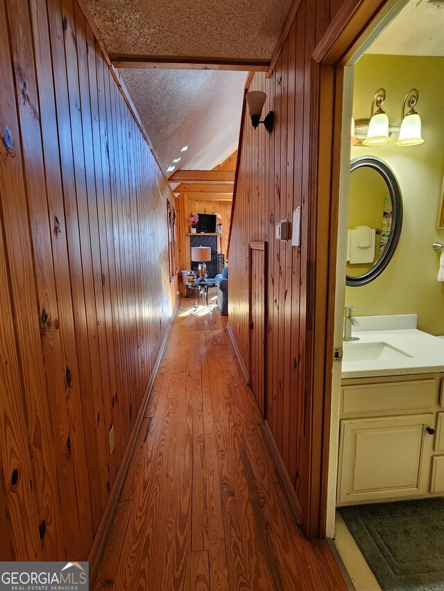 hall featuring light wood-type flooring, a textured ceiling, wooden walls, and sink