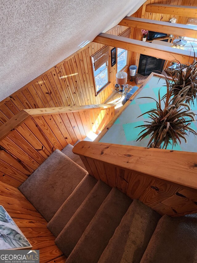 staircase with vaulted ceiling, a textured ceiling, wood walls, and hardwood / wood-style floors