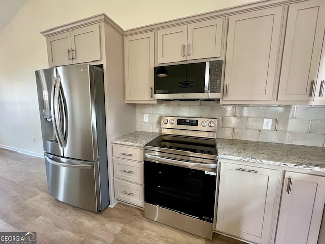 kitchen with light stone counters, cream cabinetry, stainless steel appliances, and backsplash