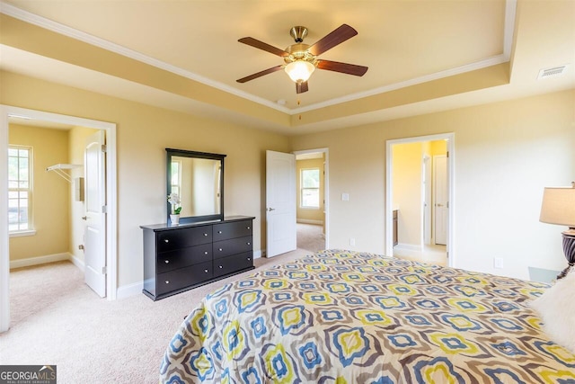 bedroom with a tray ceiling, ceiling fan, light carpet, ensuite bathroom, and ornamental molding