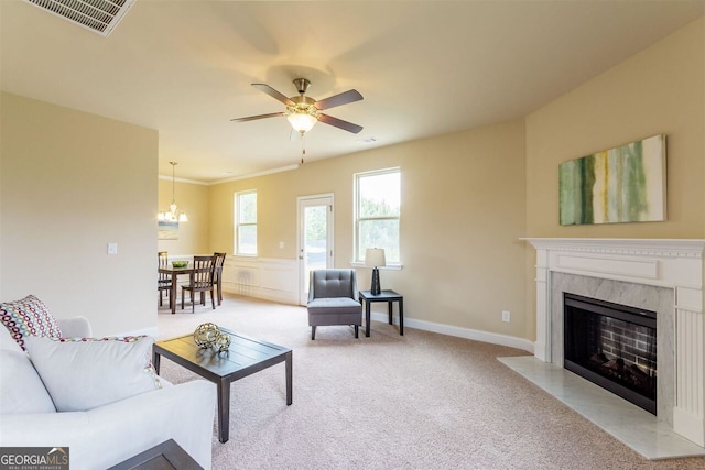 living room with a high end fireplace, ceiling fan with notable chandelier, and light colored carpet