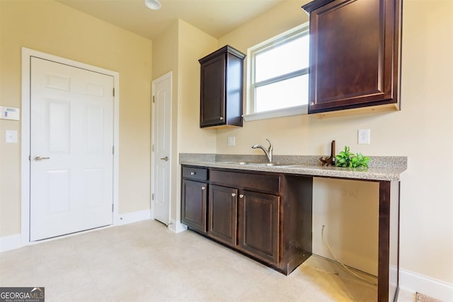 kitchen with dark brown cabinetry, light stone counters, sink, and light tile floors