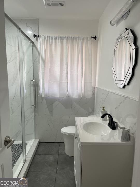 bathroom with an enclosed shower, vanity, tile walls, tile flooring, and toilet