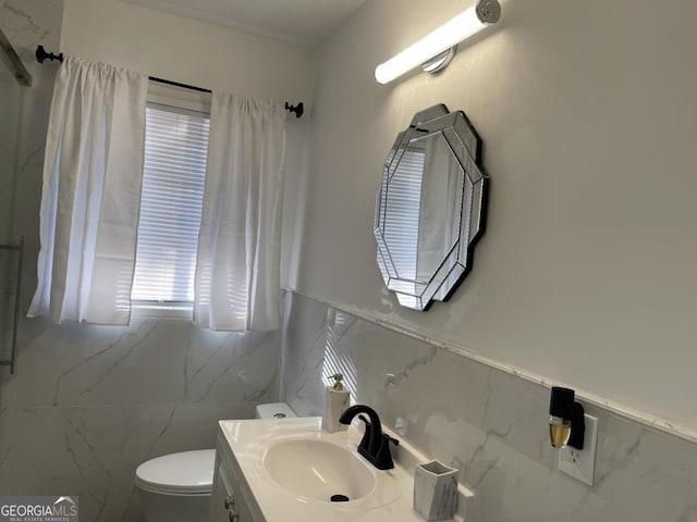 bathroom featuring tile walls, toilet, a healthy amount of sunlight, and vanity with extensive cabinet space