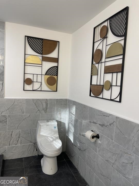 bathroom with tile floors, toilet, and tile walls