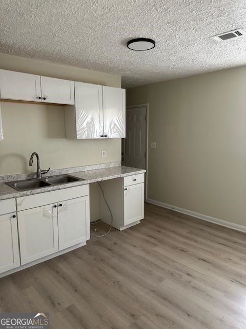 kitchen featuring a textured ceiling, sink, white cabinets, and light hardwood / wood-style flooring