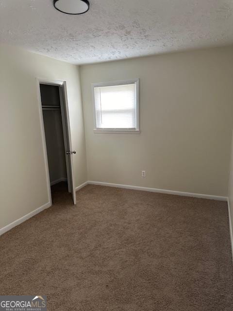 unfurnished bedroom with a textured ceiling, a closet, and dark colored carpet