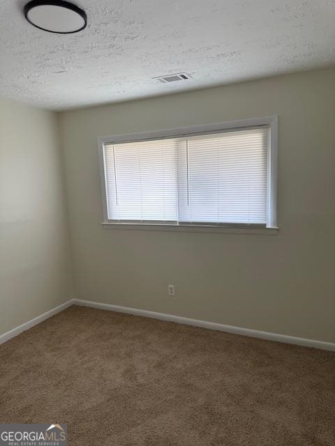 spare room with dark colored carpet and a textured ceiling