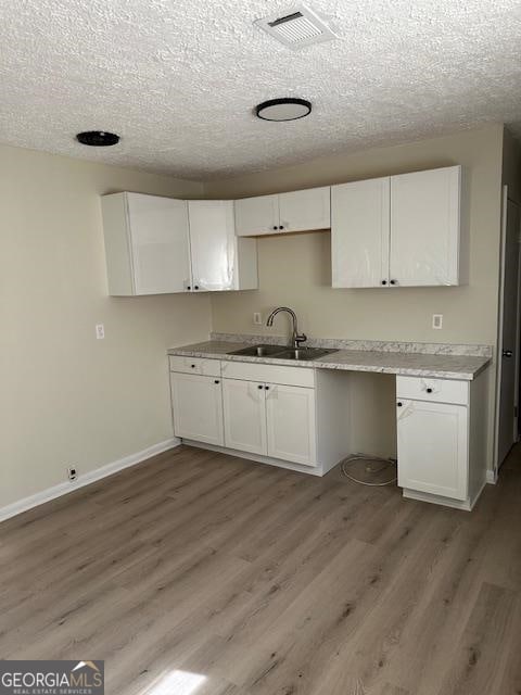 kitchen with a textured ceiling, white cabinets, sink, and light hardwood / wood-style flooring