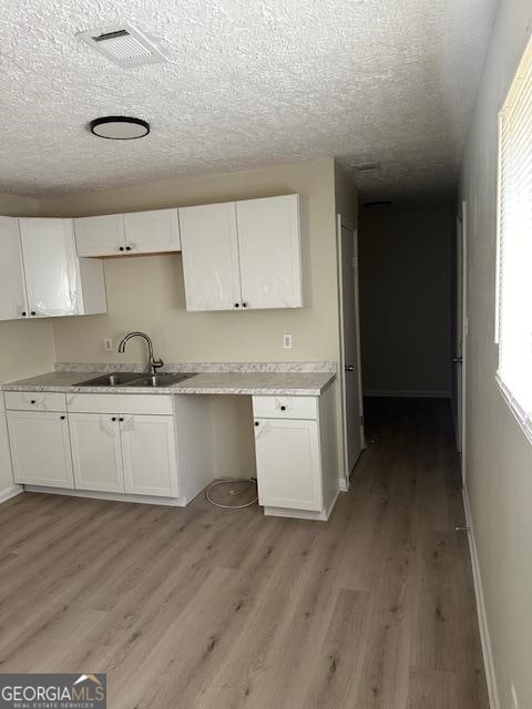 kitchen with sink, light wood-type flooring, a textured ceiling, and white cabinets