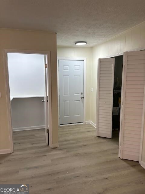 corridor with a textured ceiling and light hardwood / wood-style floors