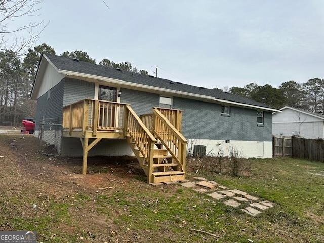 back of house featuring central AC unit, a deck, and a lawn