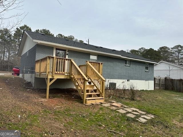 rear view of property featuring central AC, a wooden deck, and a lawn