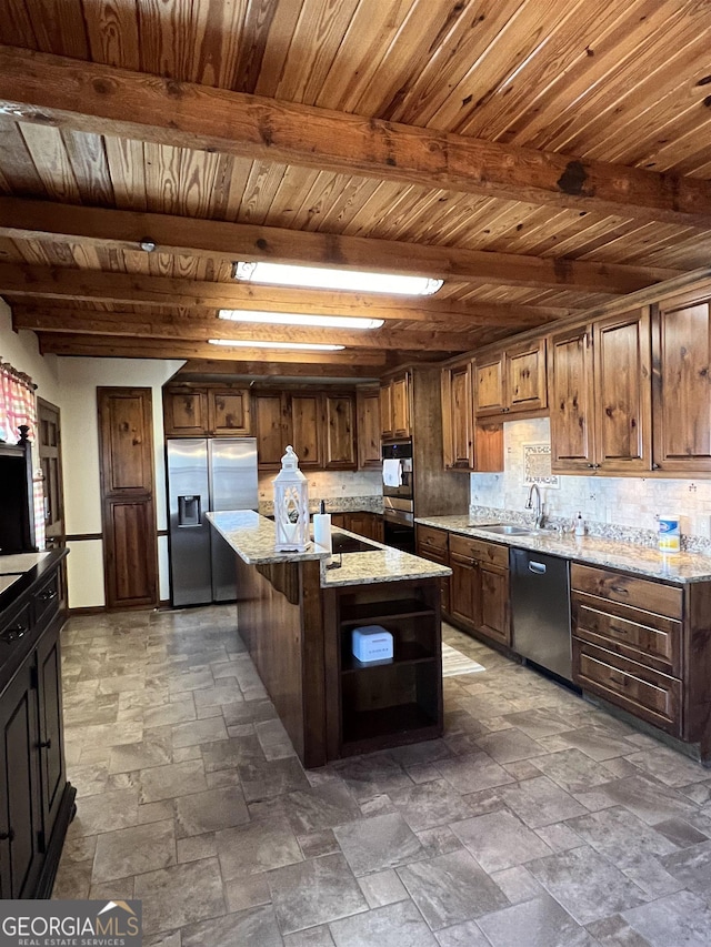 kitchen with sink, appliances with stainless steel finishes, light stone countertops, a kitchen island, and beamed ceiling