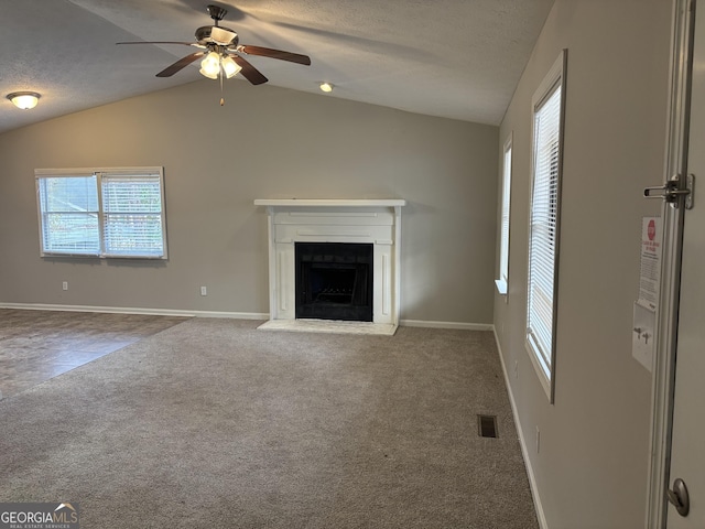 unfurnished living room featuring a textured ceiling, vaulted ceiling, a healthy amount of sunlight, and carpet flooring