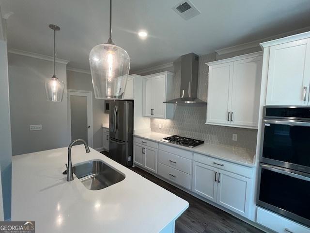 kitchen featuring appliances with stainless steel finishes, sink, decorative backsplash, wall chimney range hood, and white cabinets