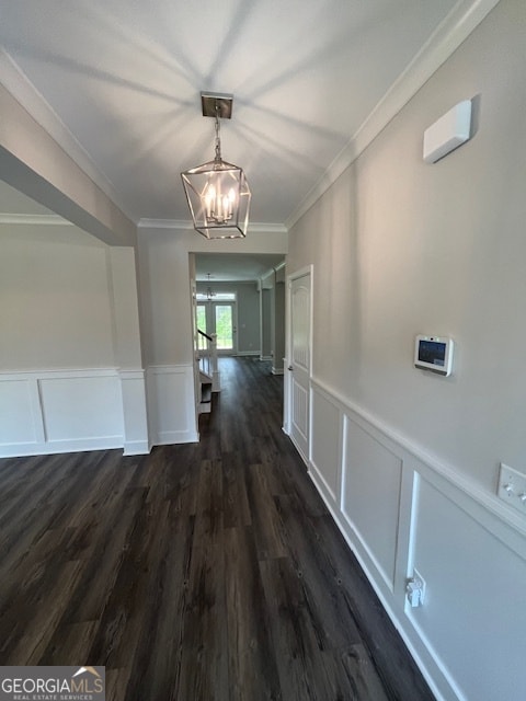 corridor with crown molding, dark wood-type flooring, and a chandelier